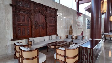Un vestíbulo con un gran panel de madera, un sofá, sillas de mimbre, una mesa de centro y una recepción.