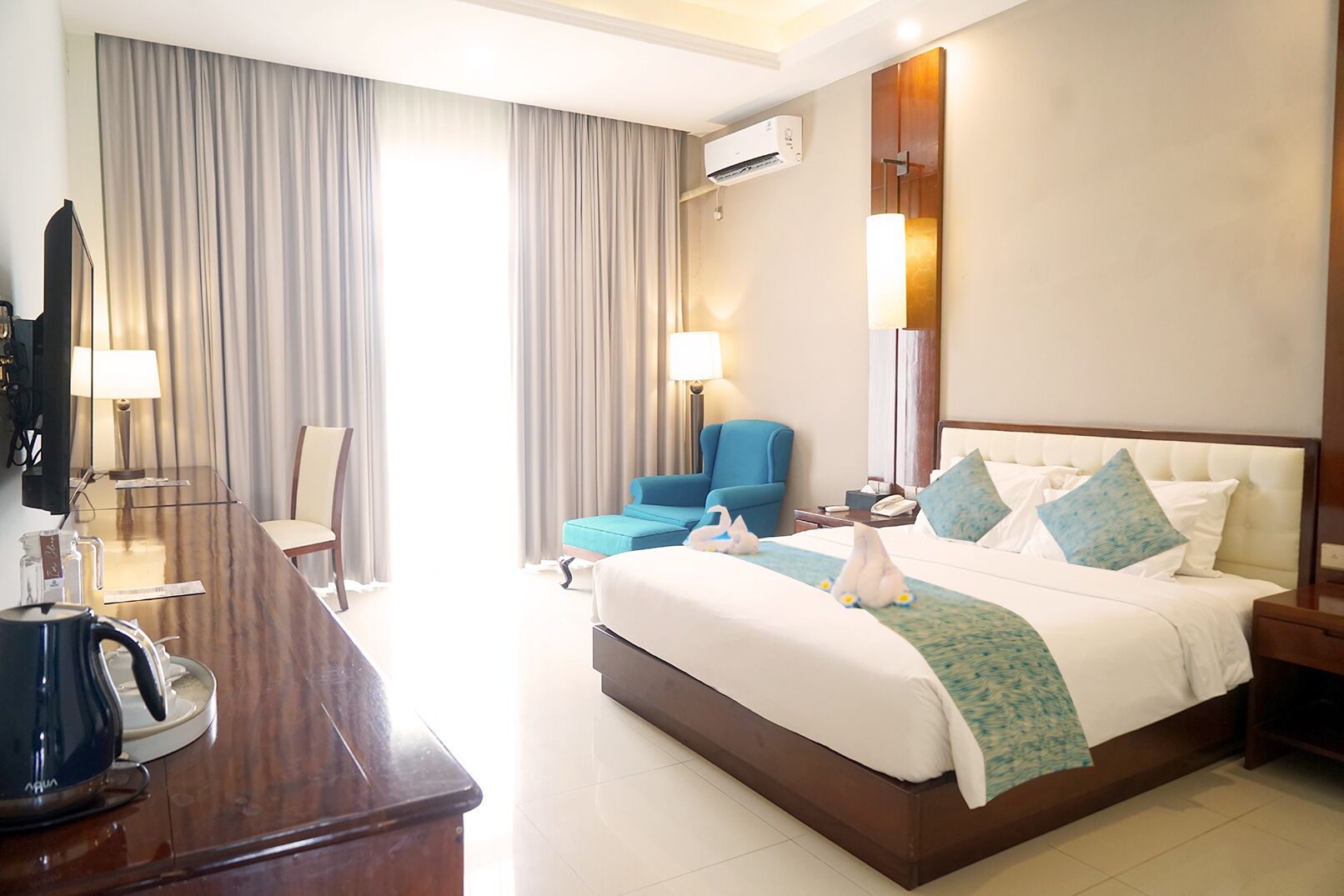 Une chambre d’hôtel avec un grand lit, un bureau avec une bouilloire, une chaise et un téléviseur.
