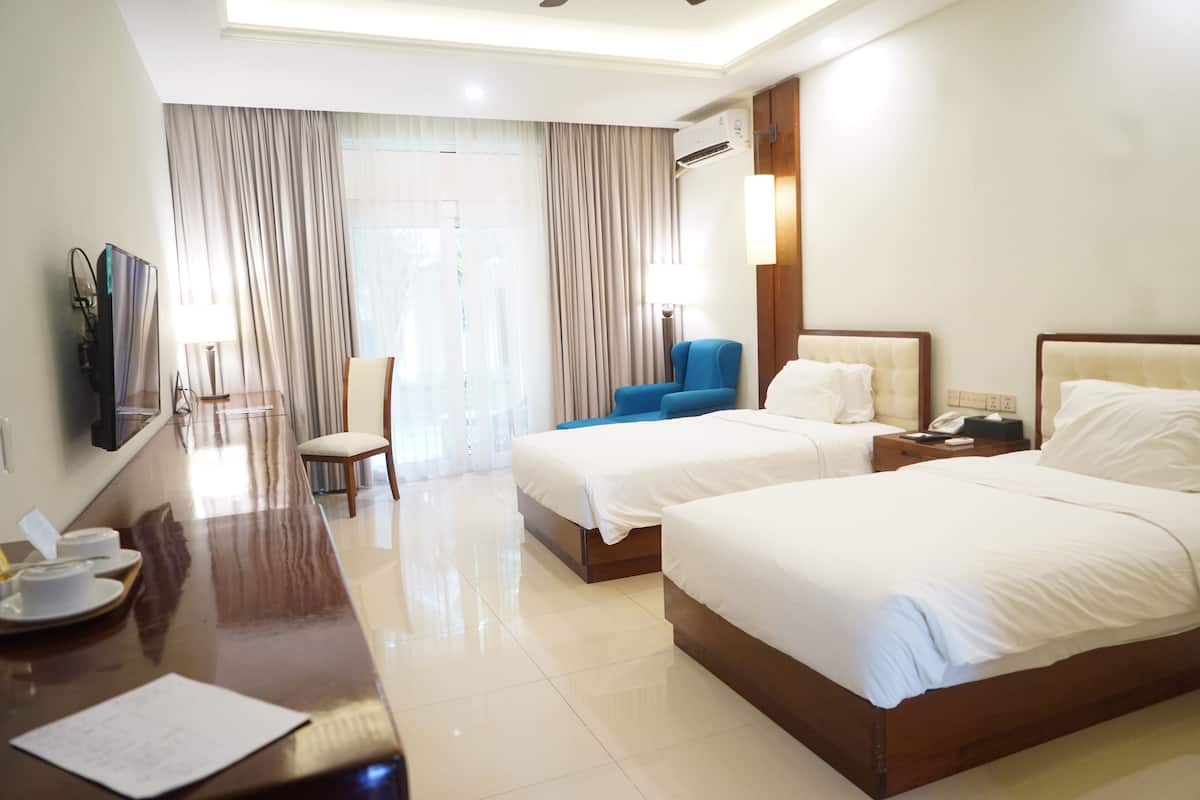 A hotel room with two beds, a desk, a chair, a TV, and a window with curtains.