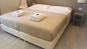 A neatly made bed with a beige bedspread and two folded towels on the footboard.