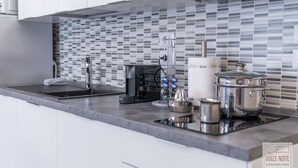 A modern kitchen with a tiled backsplash, stainless steel appliances, and a countertop with a kettle, juicer, and pots.
