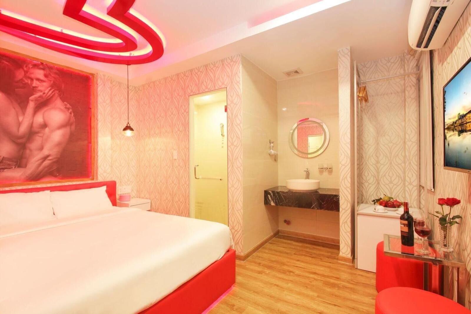 Une chambre d’hôtel moderne avec un grand lit, une salle de bain équipée d’un meuble-lavabo et une petite table sur laquelle se trouvent une bouteille et un verre.