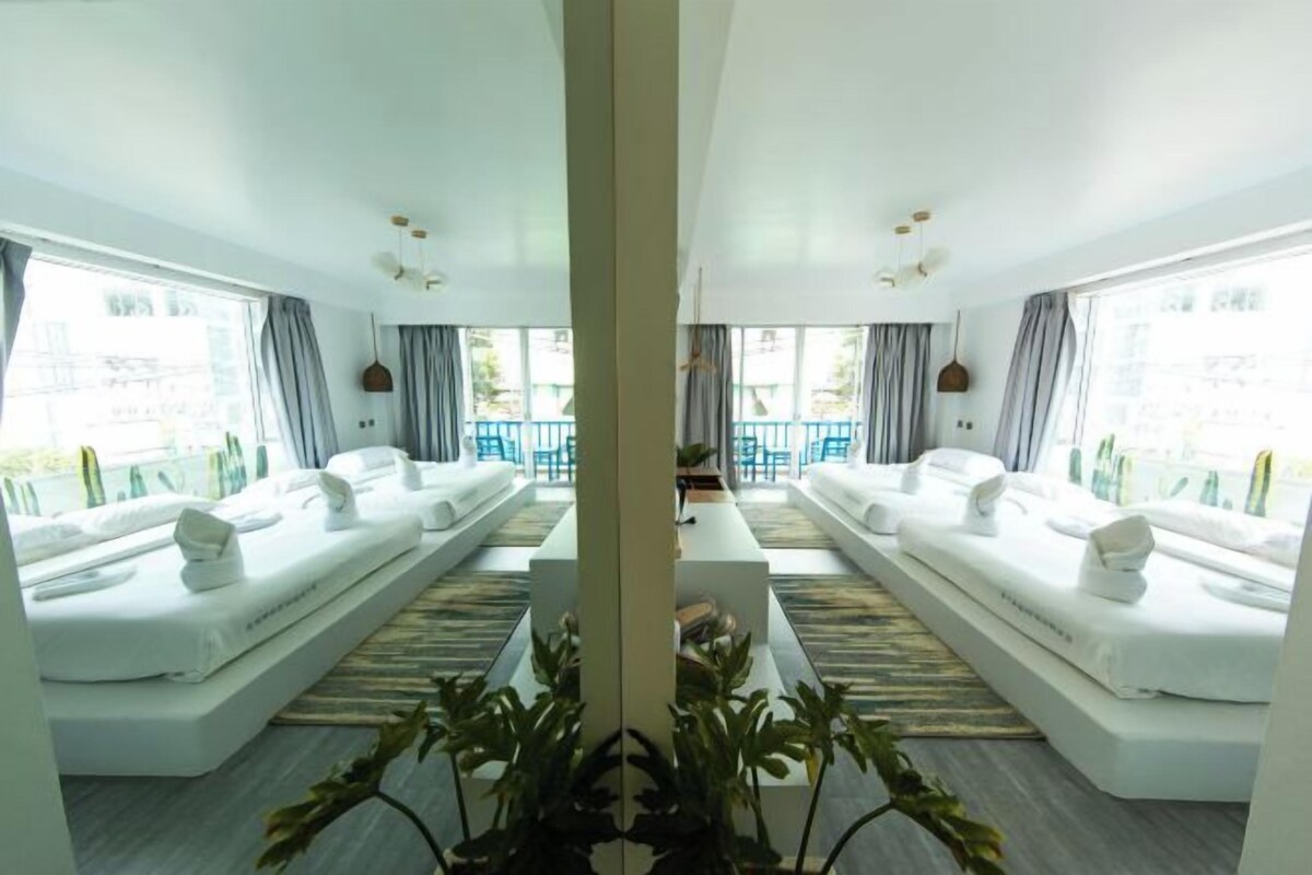 Une chambre d’hôtel moderne avec deux lits blancs, une table basse au centre et de grandes fenêtres avec des rideaux.