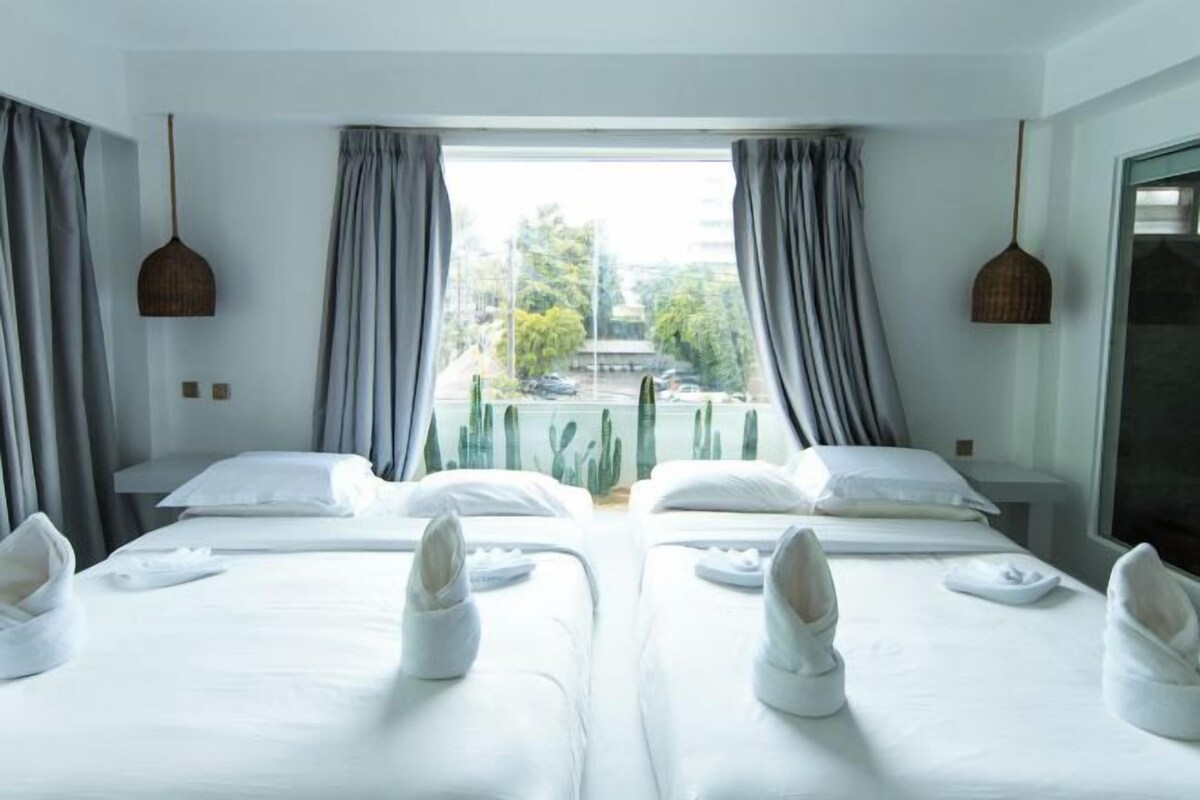 A hotel room with two beds, a large window with curtains, and a view of a building and trees outside.