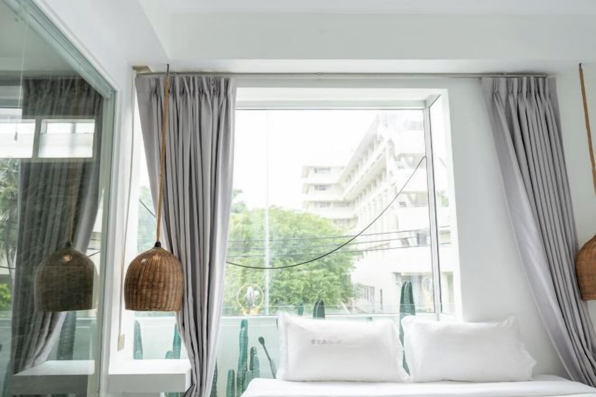 A hotel room with a bed, curtains, and a view of buildings through a window.