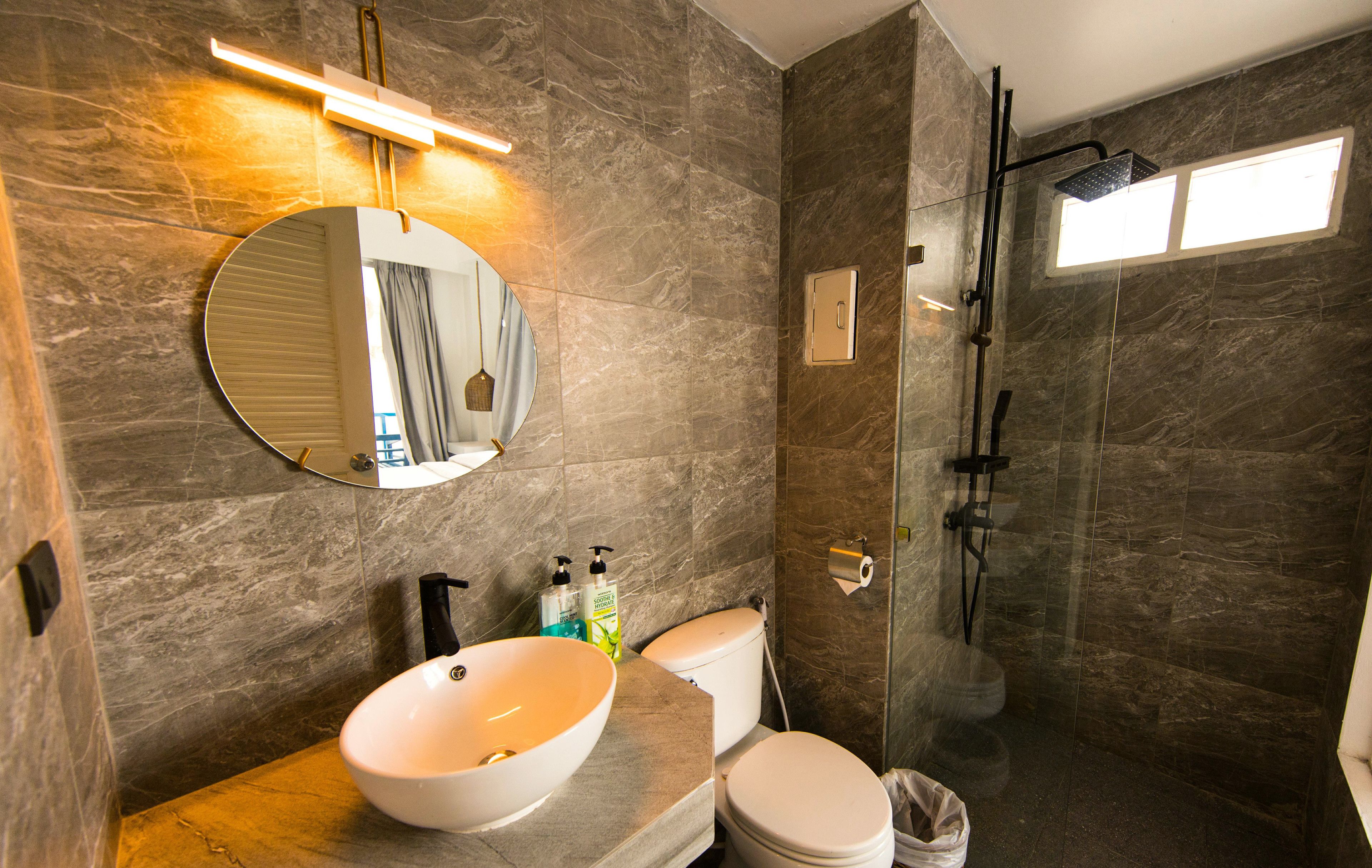 A modern bathroom with a round mirror, a sink, a toilet, and a shower.