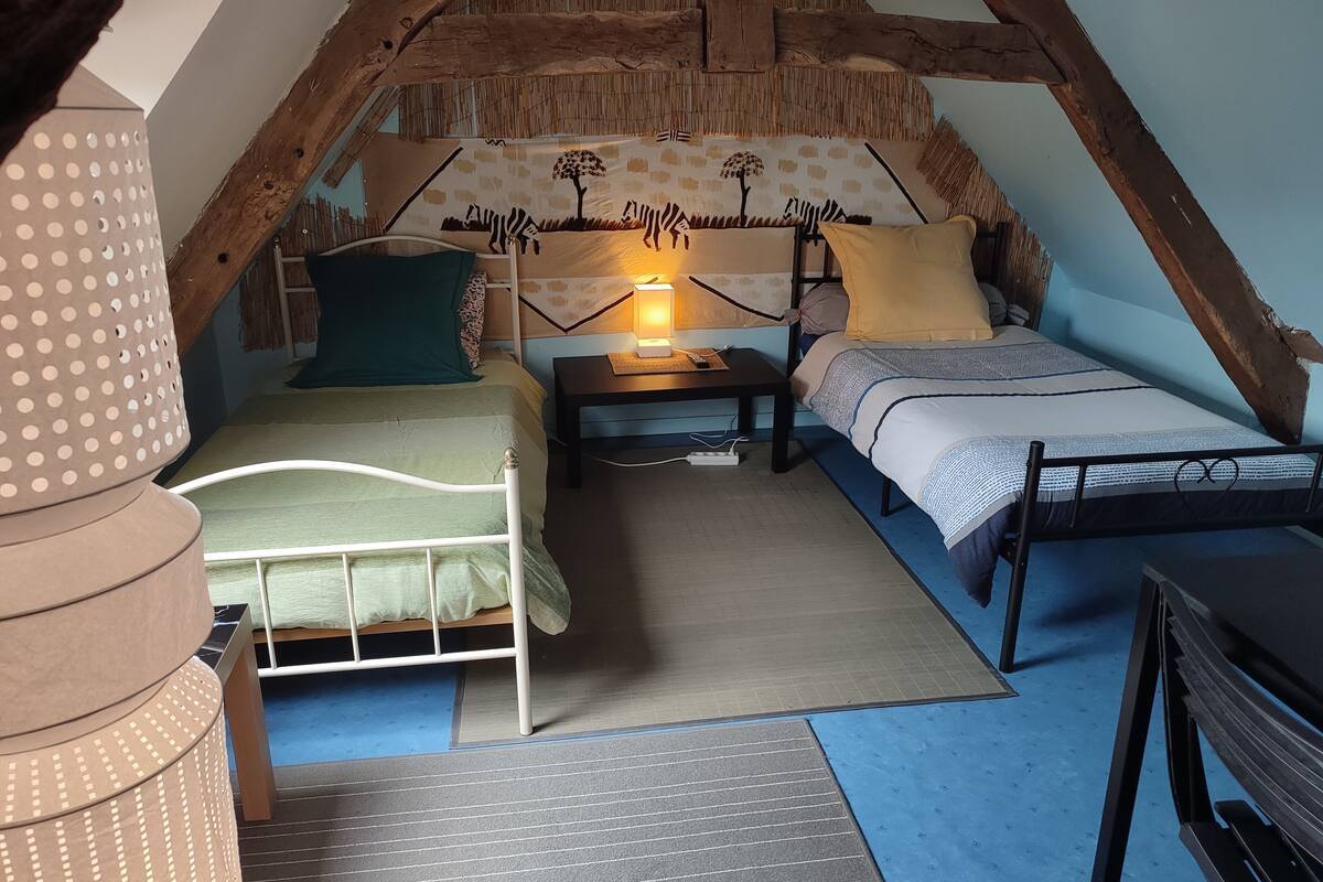 A cozy attic bedroom with a sloped ceiling, a bed with a green bedspread, a bedside table with a lamp, and a small desk.