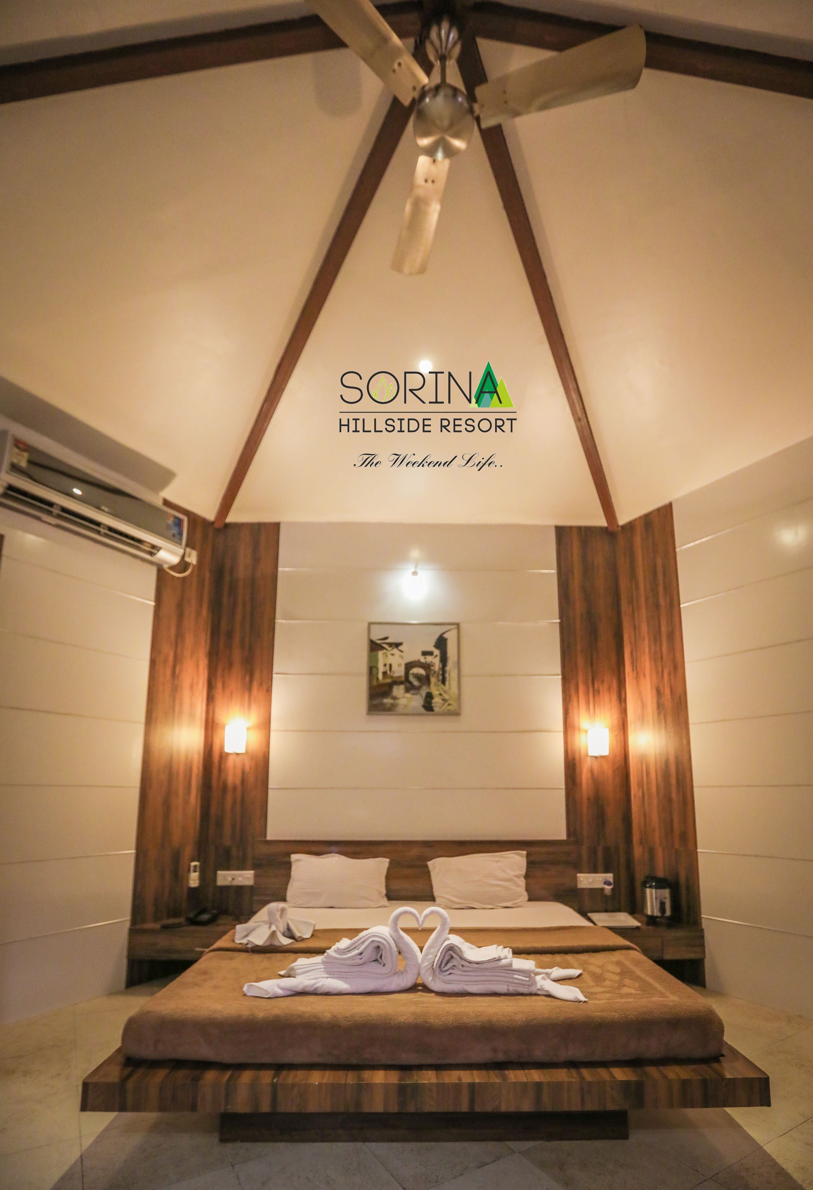 A hotel room with a large bed, wooden paneling, two wall-mounted lights, and a ceiling fan.