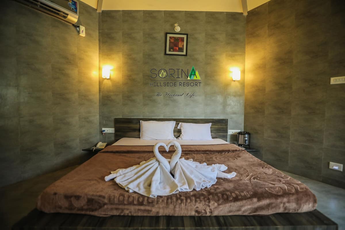 A hotel room with a bed, a wall-mounted air conditioner, and a sign reading "SORINA HILLSIDE RESORT".