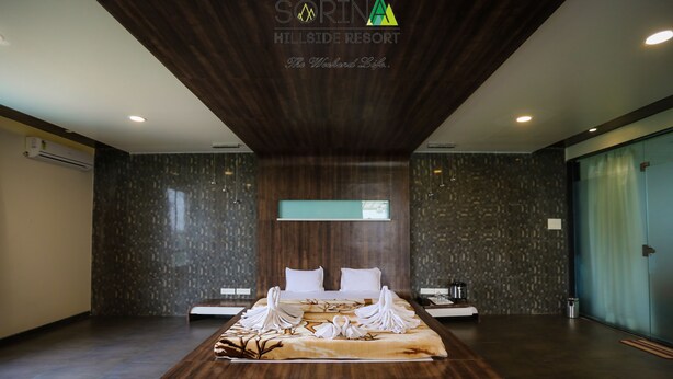 A modern hotel room with a large bed, a wooden ceiling, and a stone-textured wall. - Sorina Hillside Resort (Pune)