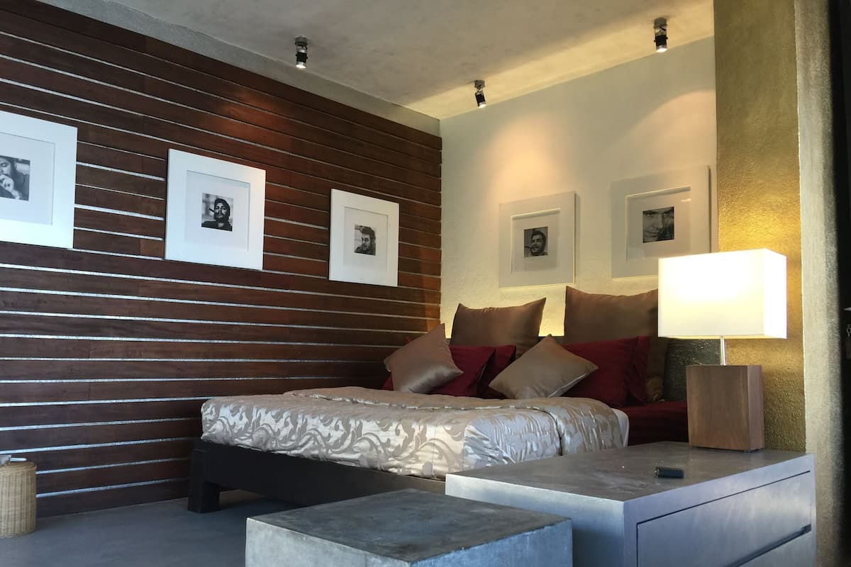 A modern bedroom with a wooden panel wall, a bed with patterned bedding, a bedside table with a lamp, and framed pictures on the wall.