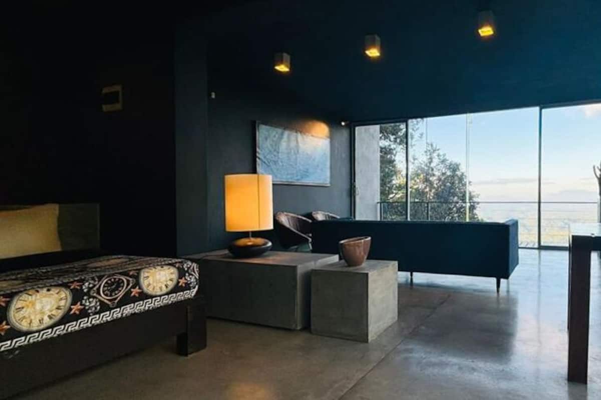 A modern room with a large window, a sofa, a chair, and a lamp.