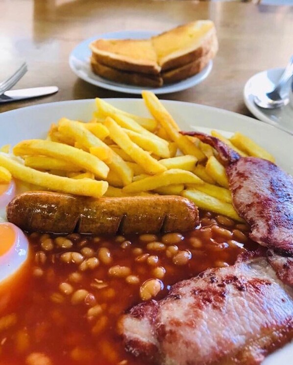 Un plato con papas fritas, salchichas, frijoles horneados y un filete a la parrilla.