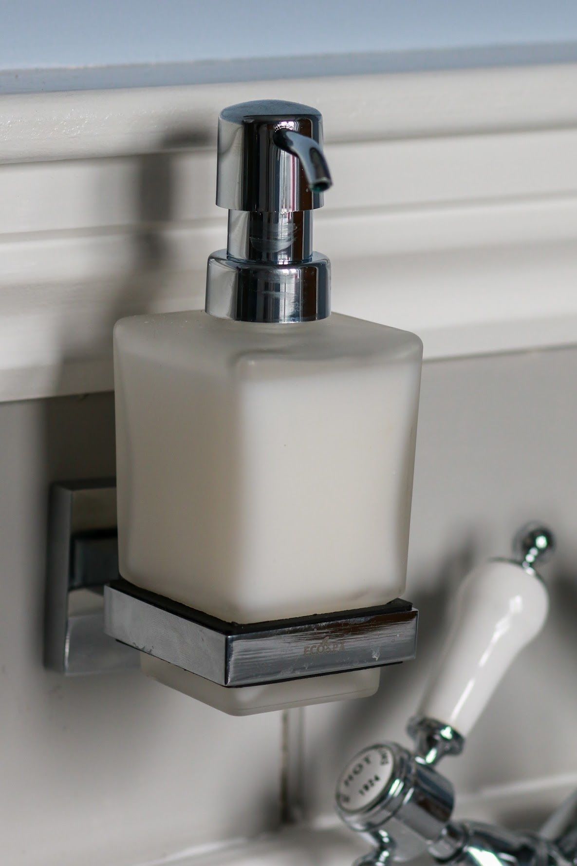 A bathroom with a white soap dispenser mounted on a wall, a chrome faucet, and a visible soap dish.