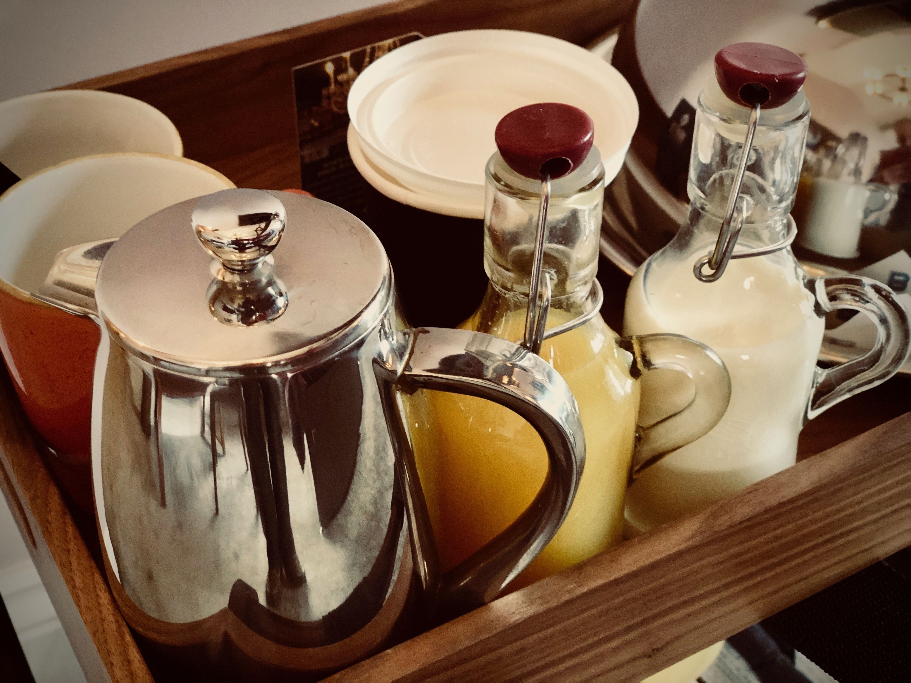 Un plateau avec une théière en argent, une bouteille en verre avec un bouchon rouge et un pichet blanc.