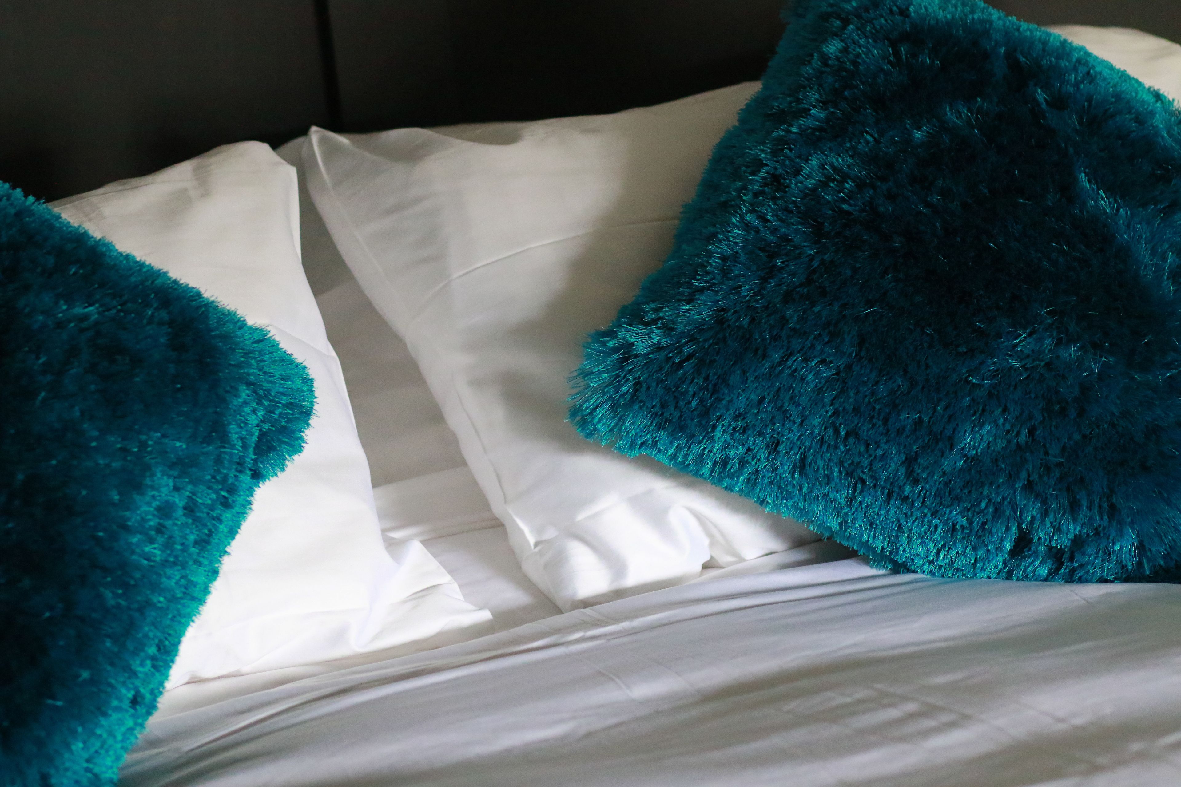A bed with white sheets and two teal pillows.