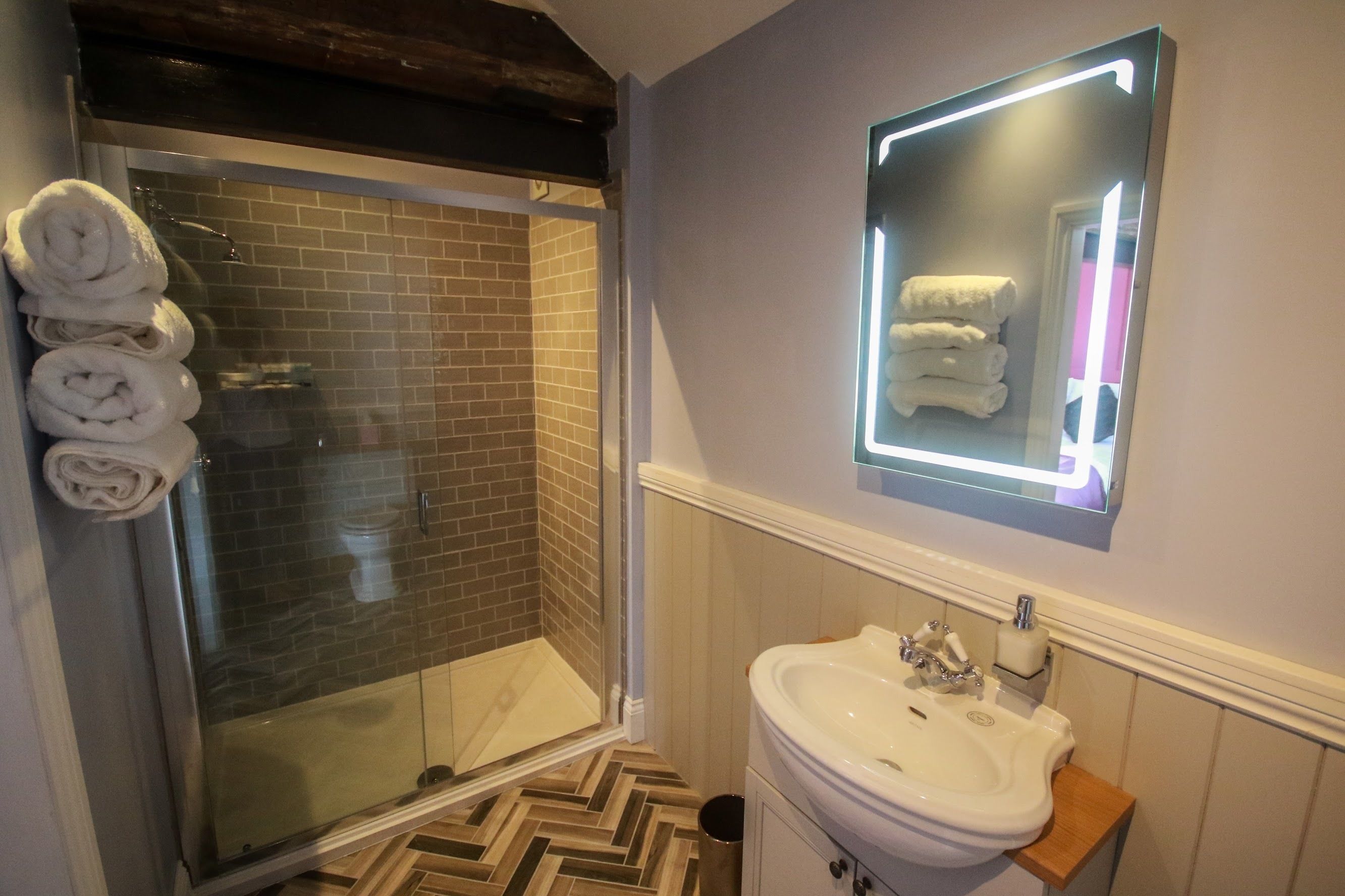 A bathroom with a glass shower, a sink, and a mirror with a light.