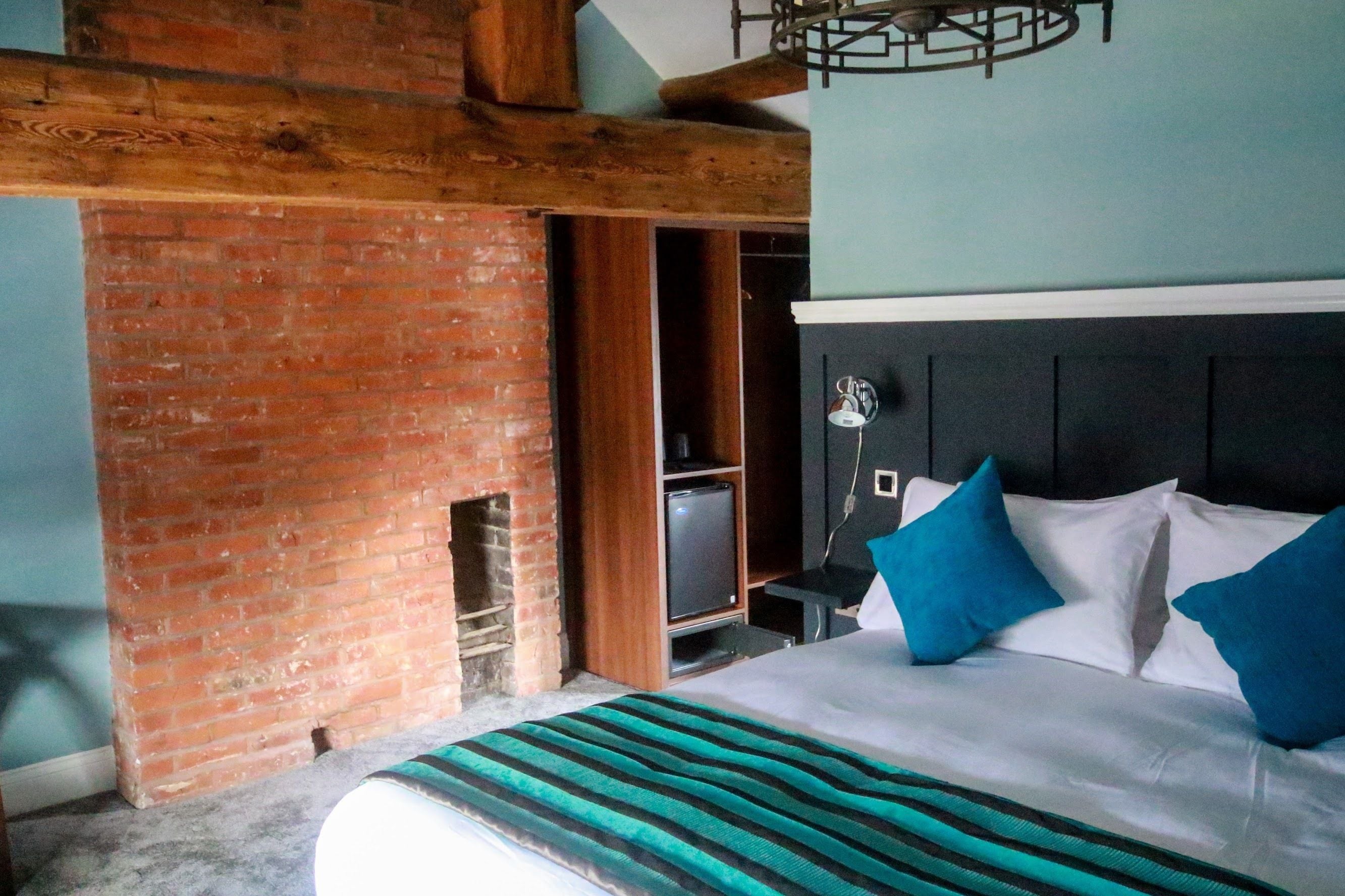 A bedroom with a brick fireplace, a bed with white and blue bedding, and a television on a wooden stand.