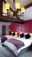 Una cama doble con cabecera roja, dos mesitas de noche y un candelabro.