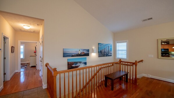 A spacious hallway with wooden flooring, a wooden staircase with a railing, and a view of a kitchen area with cabinets and a window. - Beautiful 4-BR, 3-Bath House- minutes to the Beach with onsite EV Charger (Myrtle Beach)