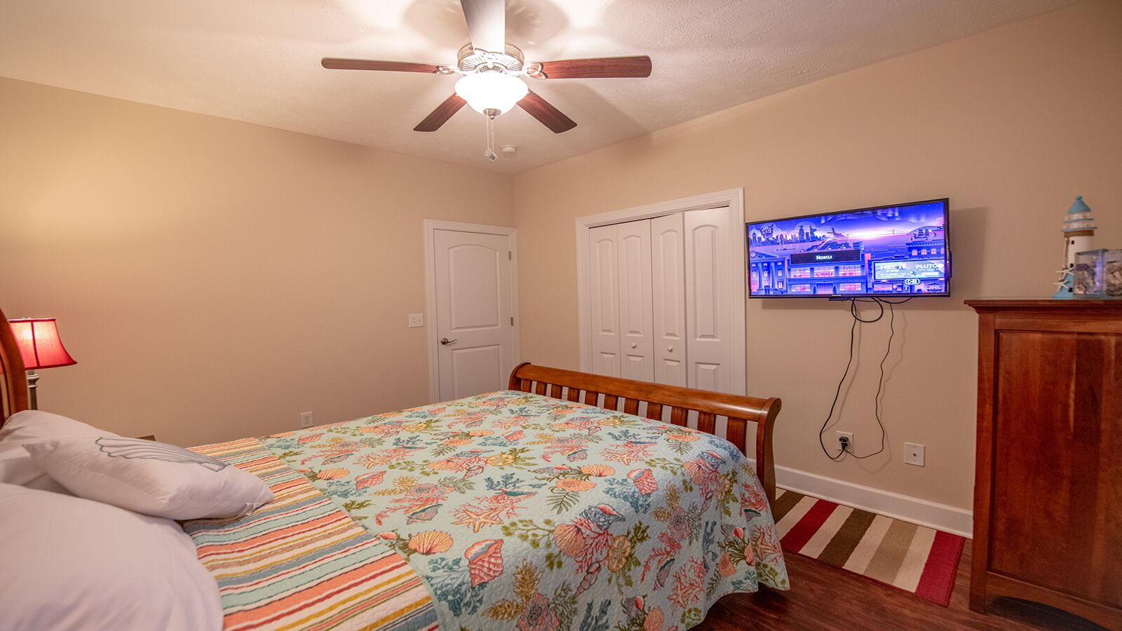A bedroom with a bed, a ceiling fan, a television, and a wooden cabinet.