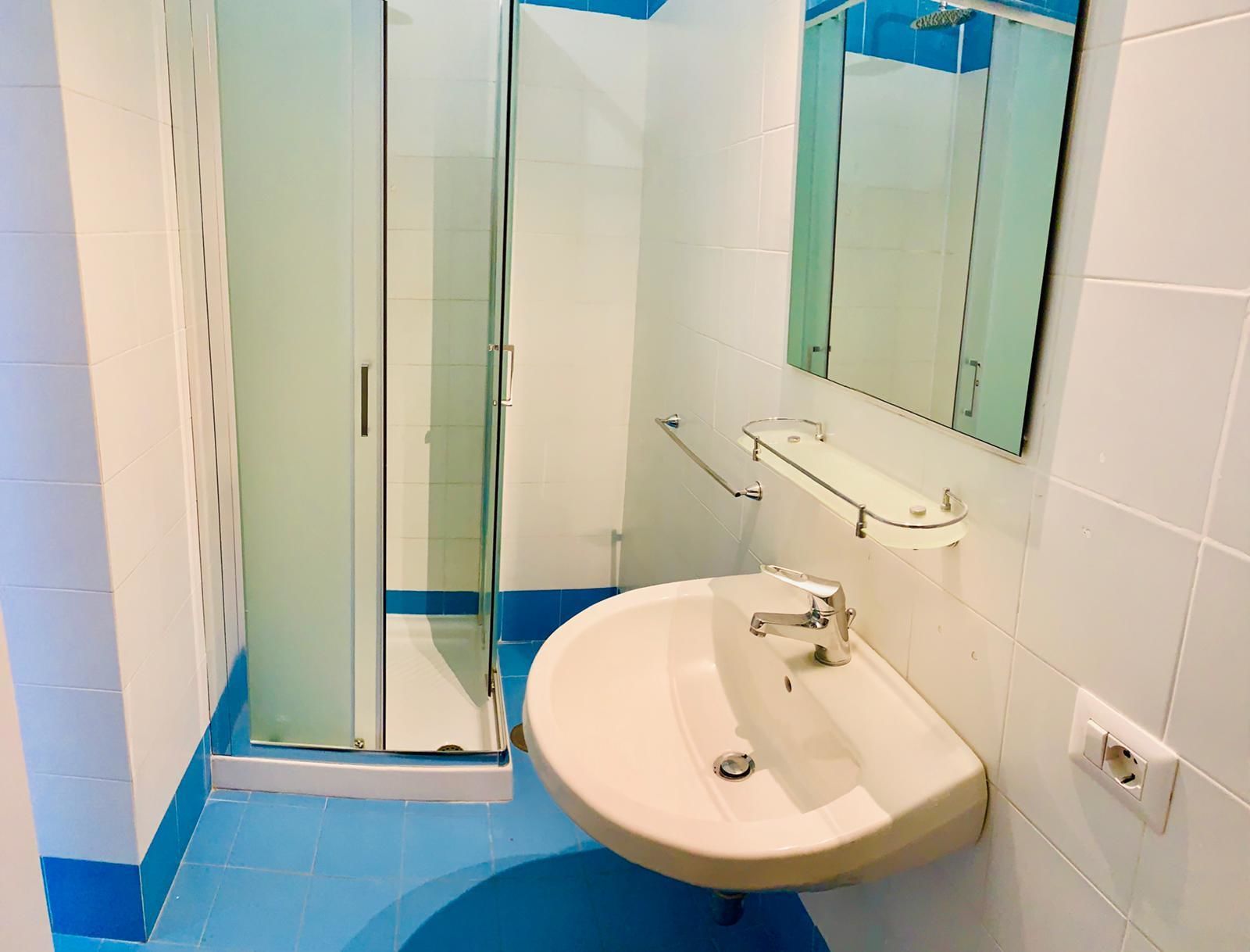 A bathroom with a glass-enclosed shower, a sink with a mirror above it, and blue-tiled flooring.