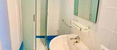 A bathroom with a glass-enclosed shower, a sink with a mirror above it, and blue-tiled flooring.