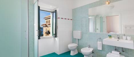 A modern bathroom with a teal floor, white fixtures, a large mirror, and a view of a building outside.