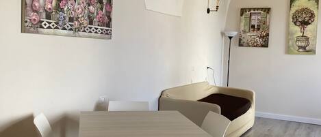 A dining area with a table and chairs, a sofa, and a painting on the wall.