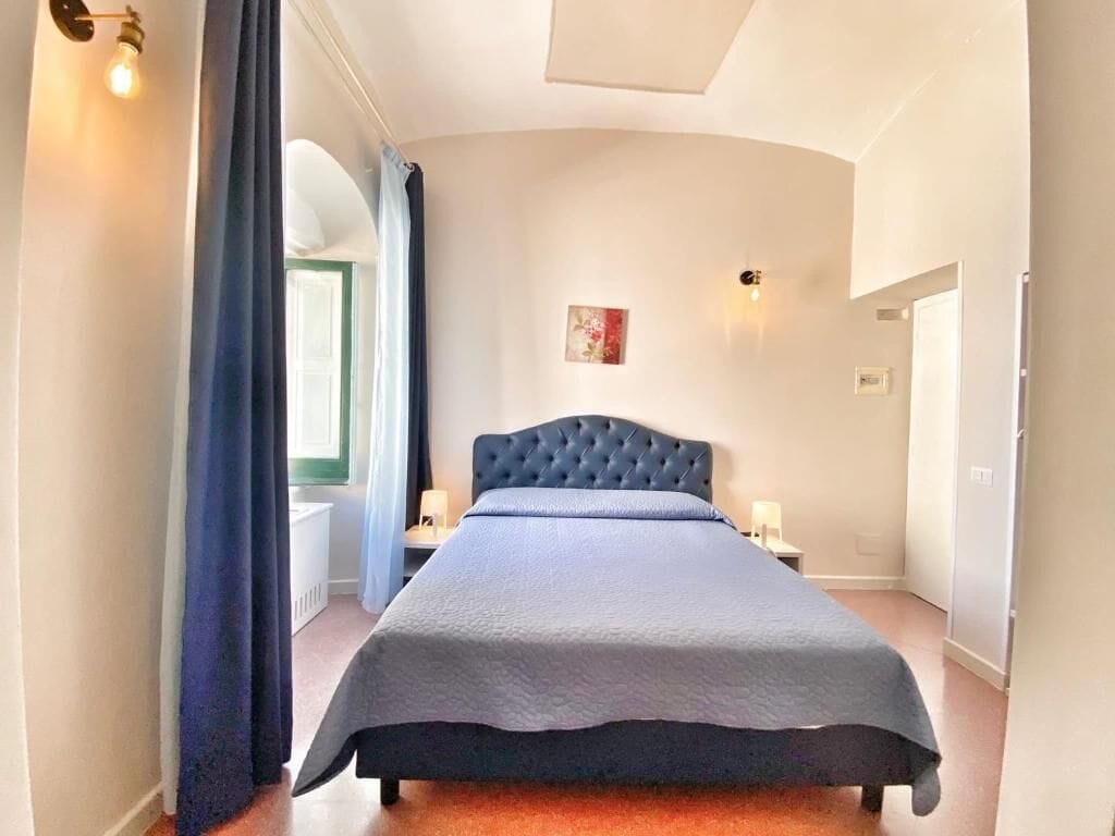 Une chambre à coucher avec un grand lit, une tête de lit capitonnée, une table de chevet avec une lampe et un tableau au mur.