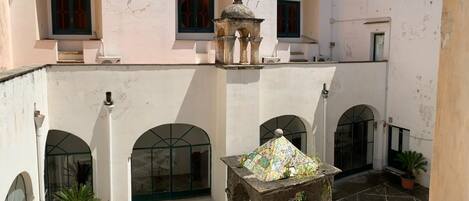 Ein Innenhof mit Fliesenboden, einer zentralen Fontäne und Rundbogenfenstern.