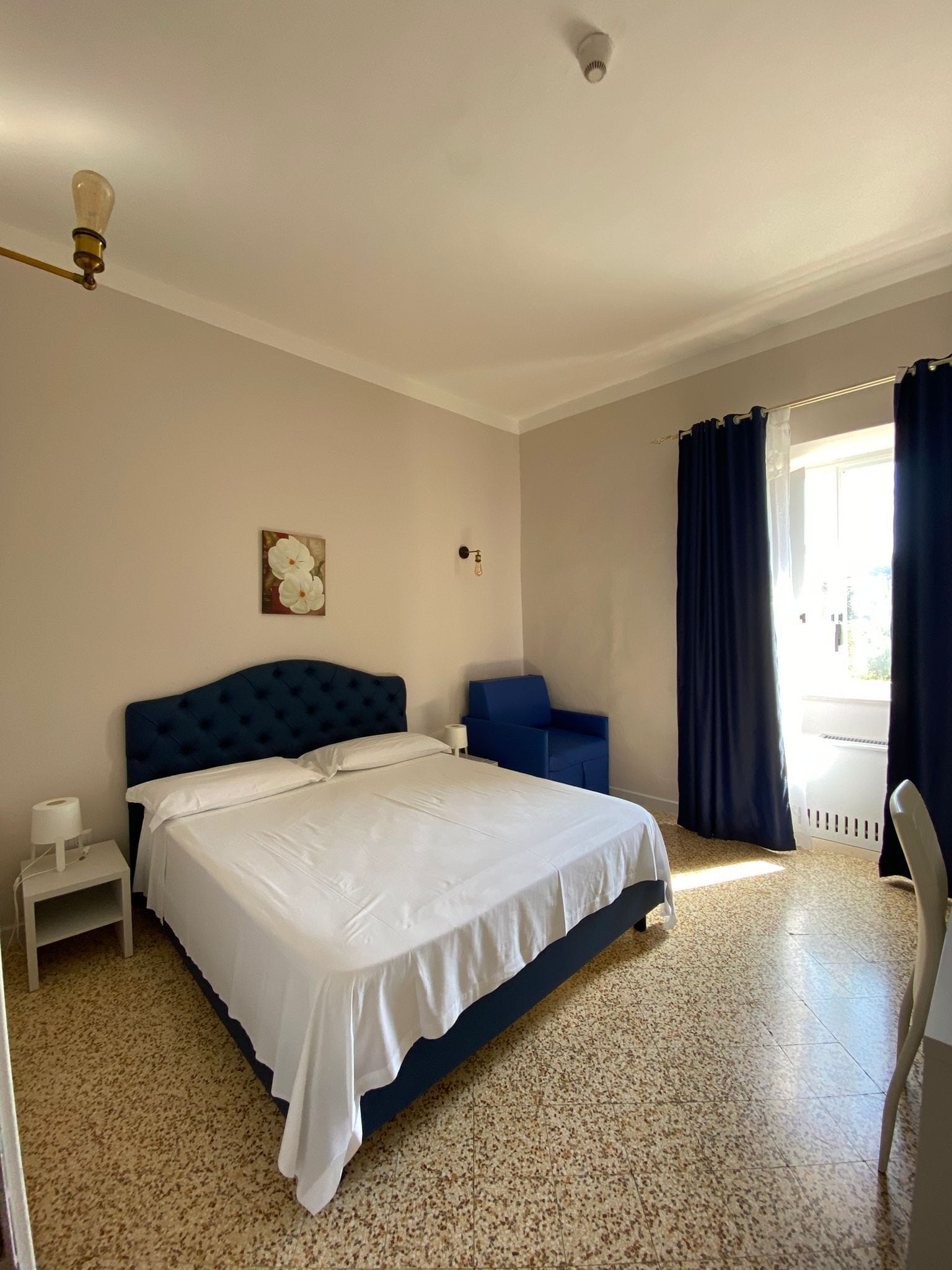 A bedroom with a large bed, a chair, a small table, and a window with curtains.
