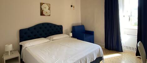 A bedroom with a large bed, a chair, a small table, and a window with curtains.