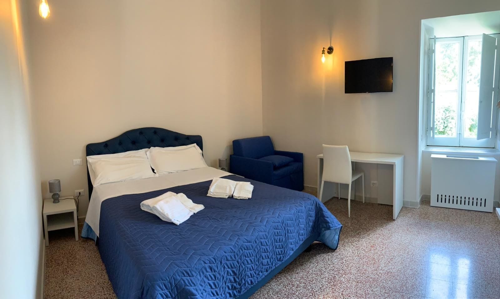 A bedroom with a bed, a chair, a desk, and a TV.