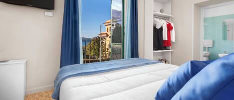 A hotel room with a bed, a TV mounted on the wall, a wardrobe, and a bathroom with a sink and mirror.