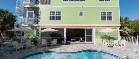 A two-story building with a swimming pool, outdoor seating, and a covered patio area.