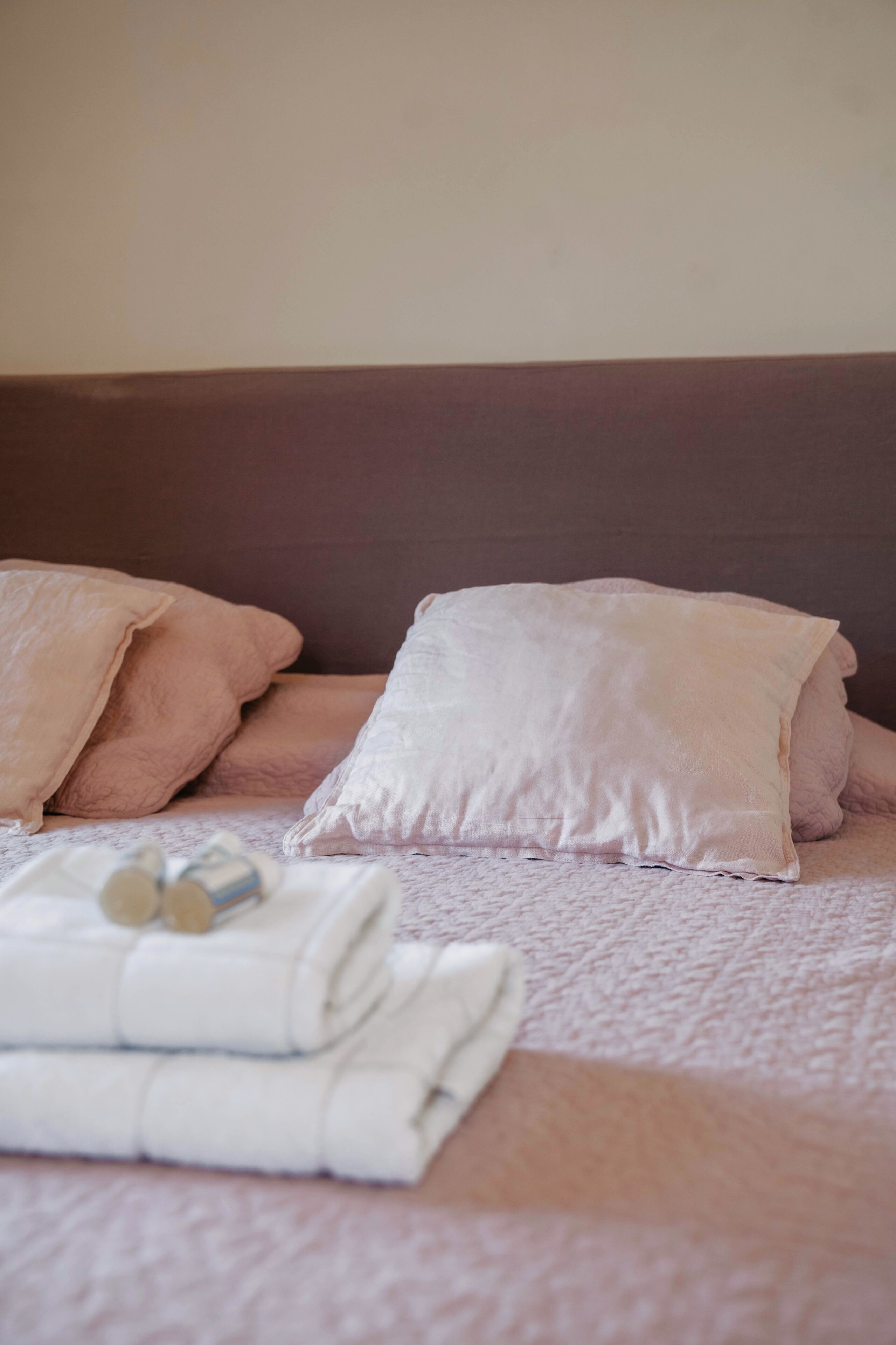 Ein ordentlich gemachtes Bett mit einer rosa-weißen Bettdecke, einem gefalteten weißen Handtuch und einer kleinen Lotionflasche.