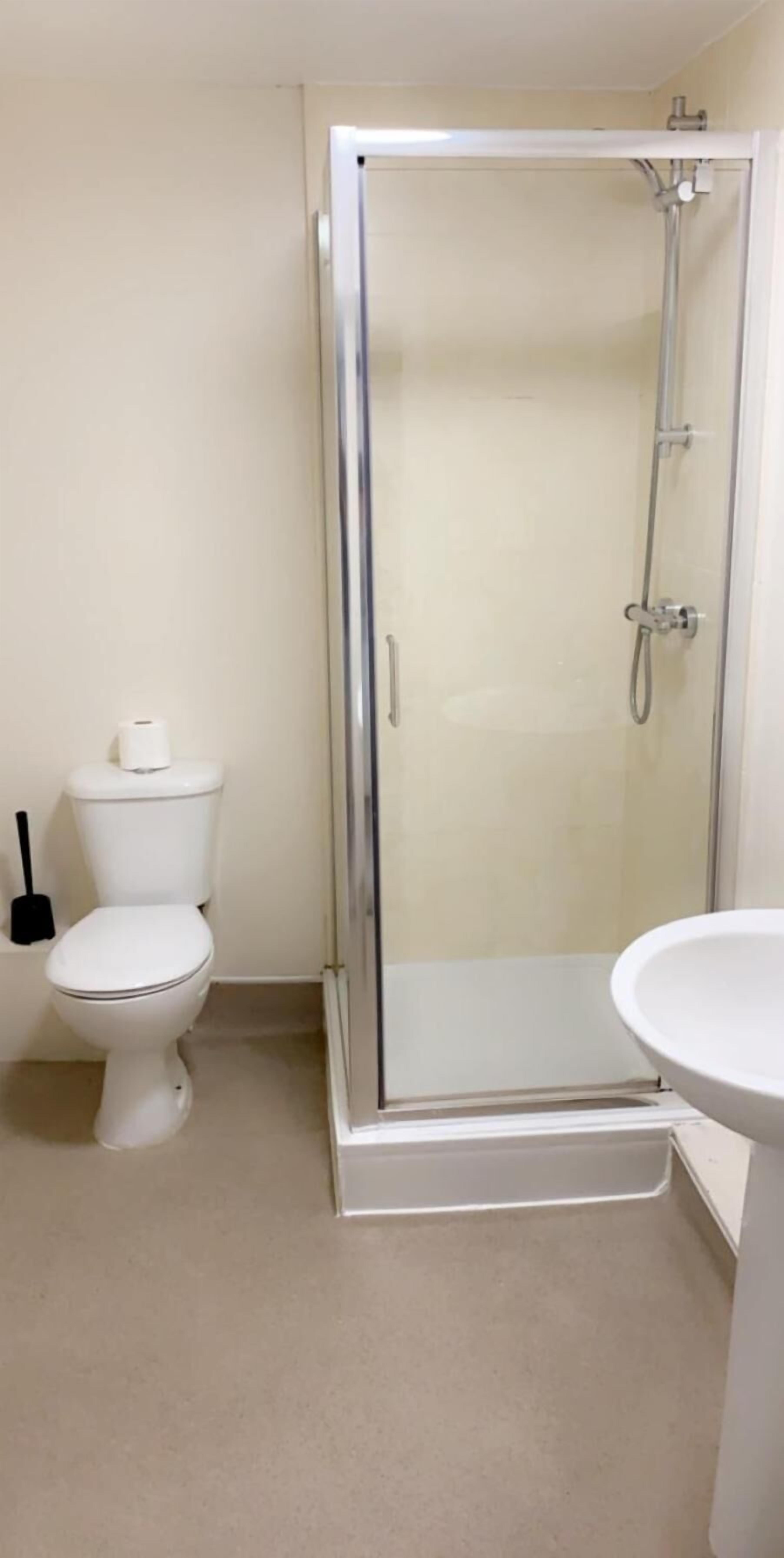Un baño con ducha vidriada, inodoro y lavamanos.
