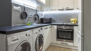 A compact kitchen with a Bosch washing machine, a microwave, and a built-in oven. - Penmoor Chance - Old Town (Bratislava)