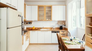 Cocina compacta con armarios blancos, horno integrado y comedor con mesa de madera lista para cuatro.