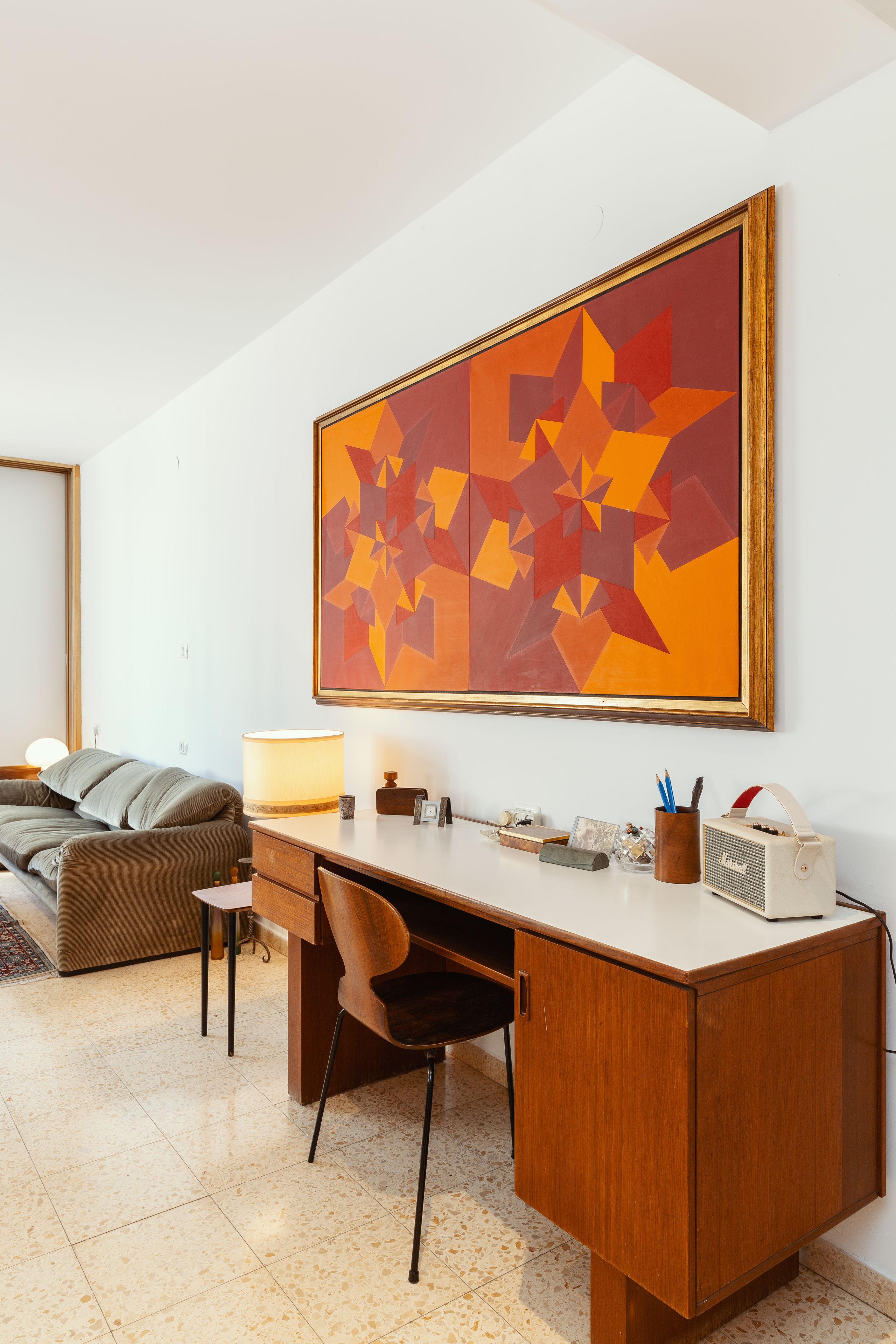 A modern living room with a wooden desk, a comfortable sofa, and a large abstract painting on the wall.