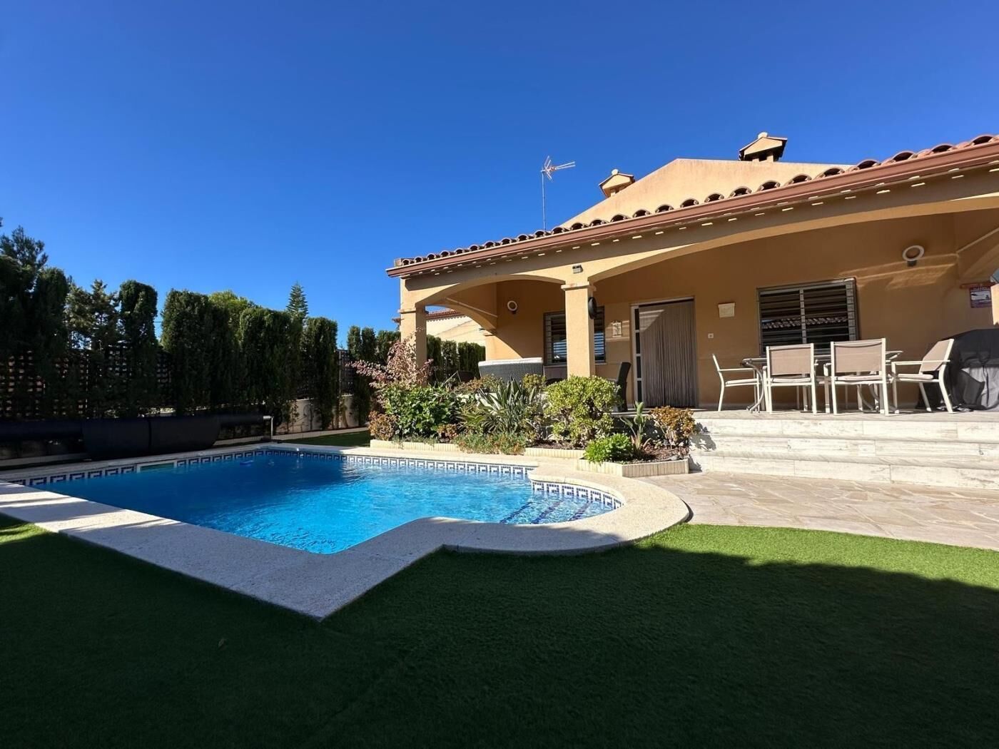 Uma casa com piscina, móveis de varanda e gramado bem cuidado.