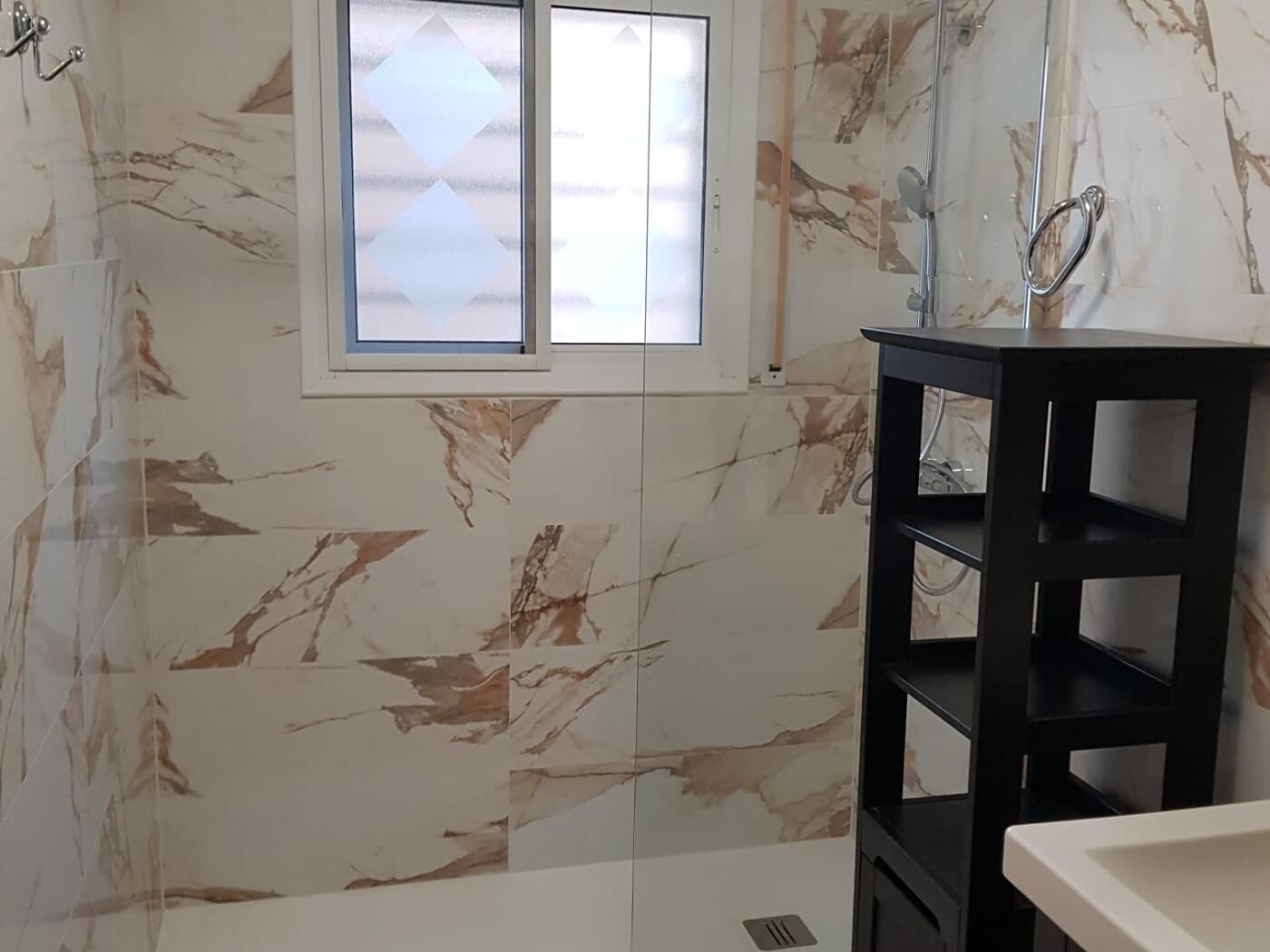 A bathroom with marble walls, a black shelf, and a window with frosted glass.