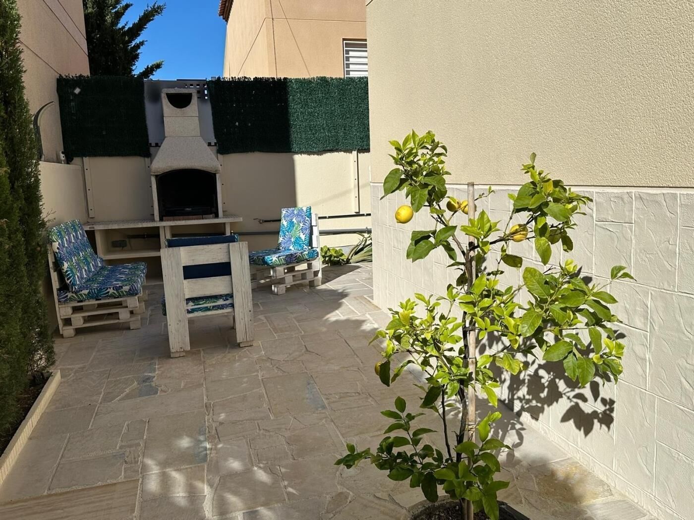 A patio with a barbecue grill, two chairs, and a potted lemon tree.