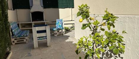 A patio with a barbecue grill, two chairs, and a potted lemon tree.