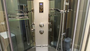 A modern glass-enclosed shower stall with a built-in seat, a handheld showerhead, and a control panel.