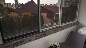 A balcony with two chairs, a small table with a potted plant, and a view of buildings and trees.