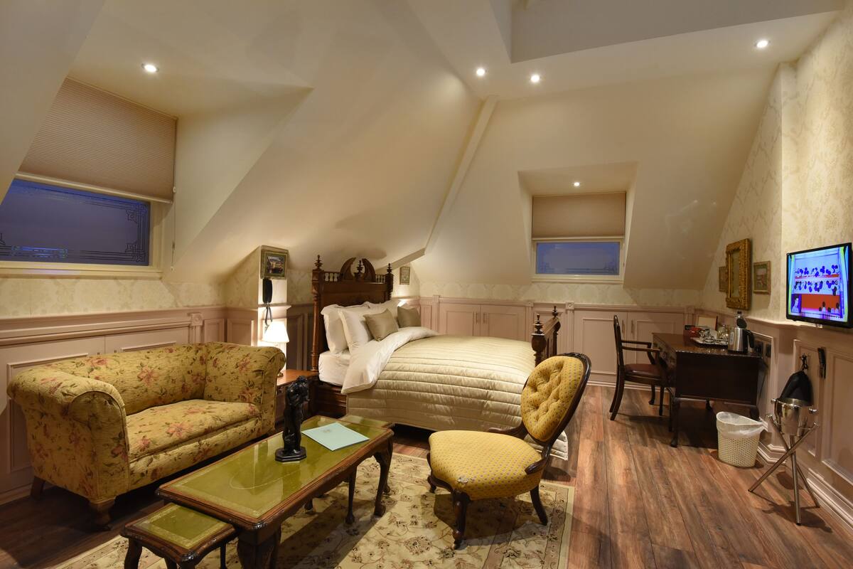 A bedroom with a bed, a chair, a sofa, a desk, and a television.
