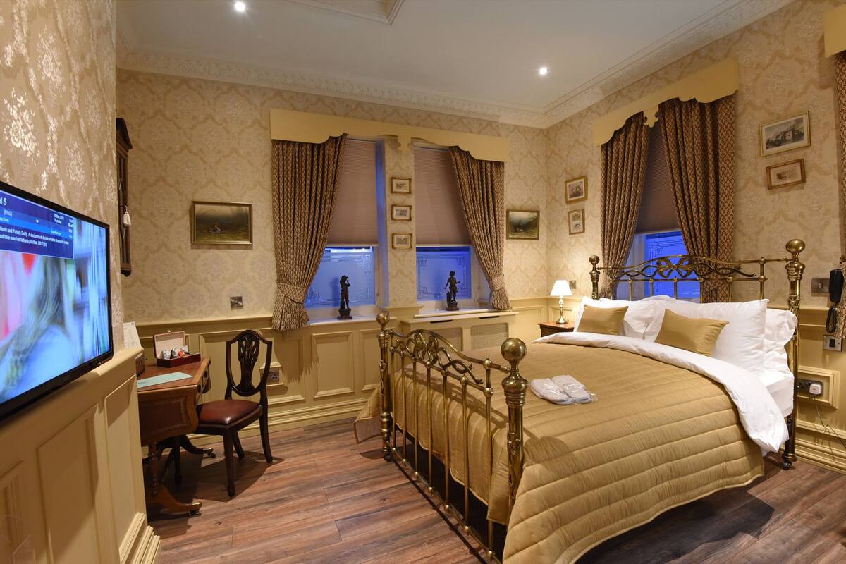 A hotel room with a large bed, a desk with a computer, a chair, and a television.