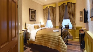 A hotel room with a bed, a bedside table, a clock, and a window with curtains. - The Aston Tavern (Birmingham)